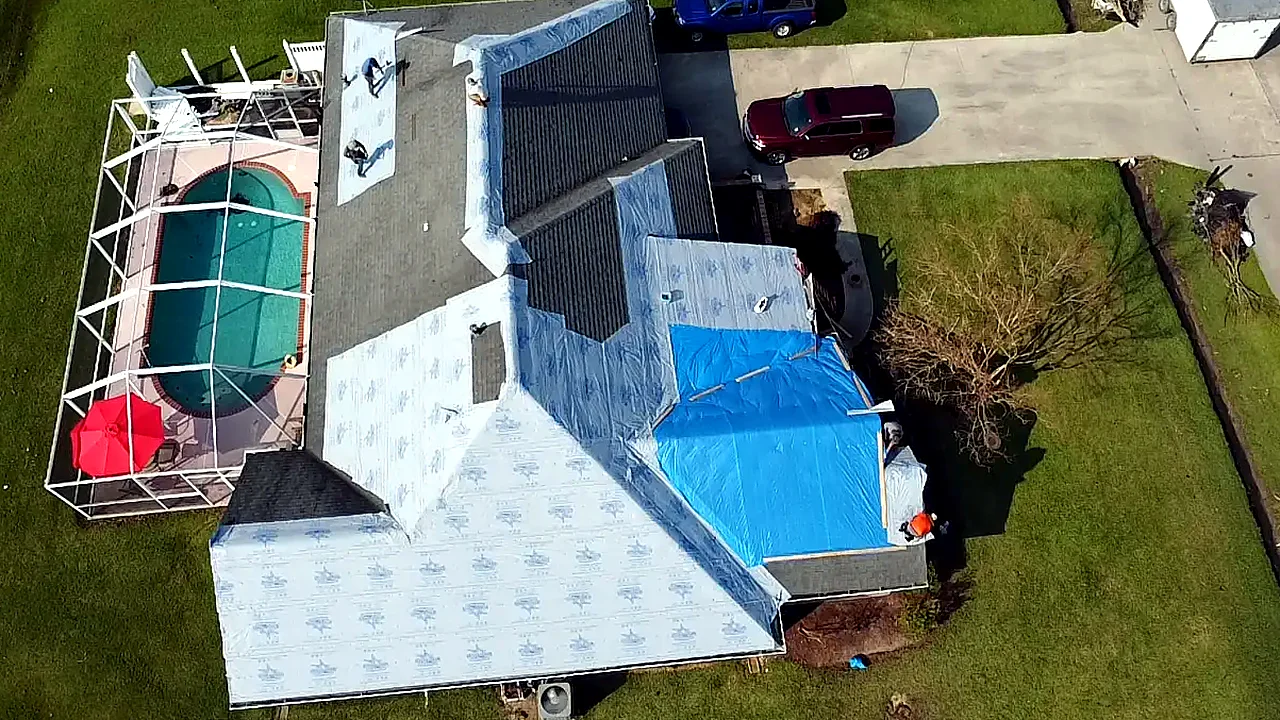Aerial view of a storm-damaged roof with underlayment and a blue tarp